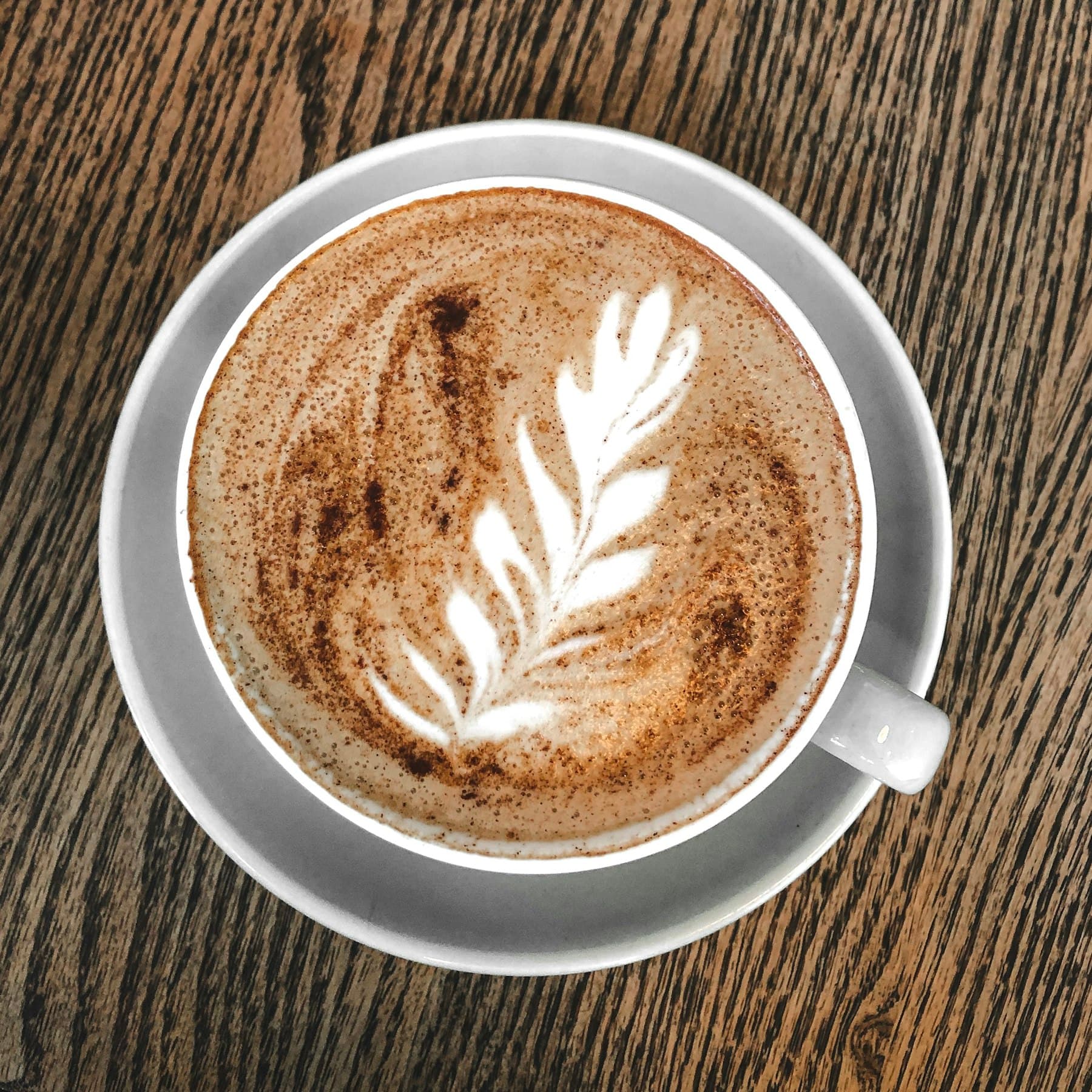 Xícara de café com latte art em formato de folha, vista de cima sobre uma mesa de madeira
