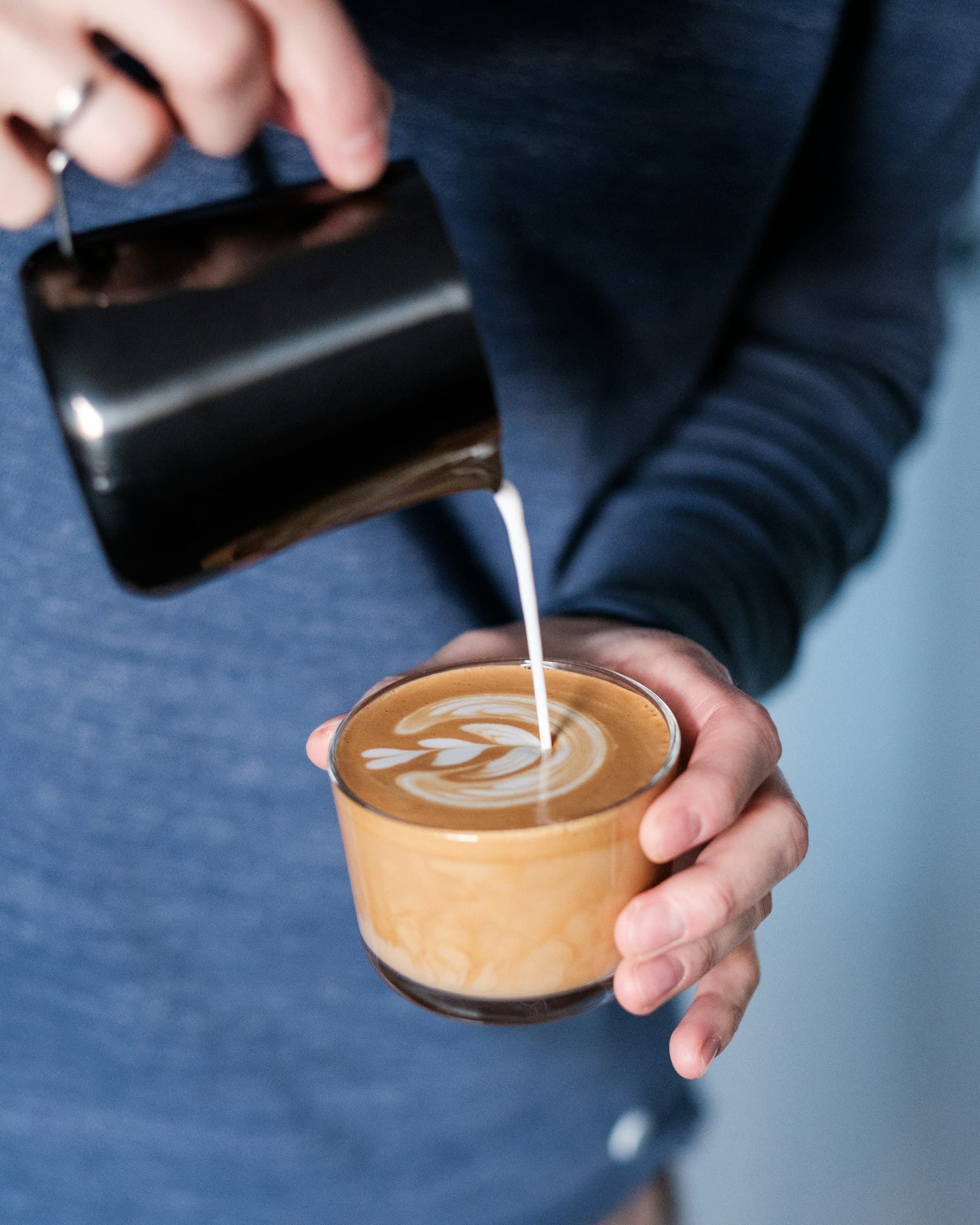 Leite sendo servido devagar sobre um espresso, desenhando a base de um latte art